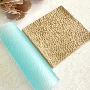 Könnte beinhalten: Ein hellblauer, strukturierter Nudelholz und eine beige, strukturierte Fondantplatte.