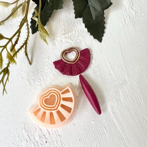 Peut inclure: Trois moules en argile polymère pour la fabrication de boucles d'oreilles. Les moules sont en forme de demi-cercle avec un motif de cœur au centre. Les moules sont roses, pêche et bordeaux.
