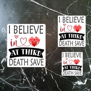 May include: Three white stickers with black text and red hearts. The text on each sticker reads "I believe in at third death save". Each sticker features a red 20-sided die with a white "20" inside.