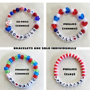 May include: Four beaded bracelets featuring red, white, and blue color schemes. Three bracelets use chunky plastic beads with letter cubes spelling GO PHILS, PHILLIES, and PHANATIC. One bracelet uses red and white clay discs spelling PHILLIES.