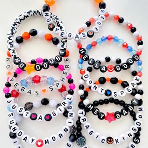 May include: A collection of beaded bracelets in various colors, featuring white letter beads spelling out phrases like "NO DOUBT," "VEGAS," and "HELLA GOOD." Some bracelets include star, heart, and smiley face charms. The text "BRACELETS ARE SOLD INDIVIDUALLY" is at the bottom.