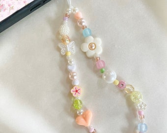 May include: A pastel-colored phone charm with a variety of beads, including pearls, hearts, flowers, and butterflies. The charm is attached to a black phone case.
