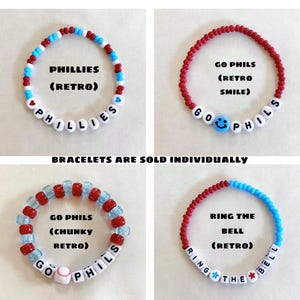 May include: Four beaded bracelets with white letter beads spelling "PHILLIES", "GO PHILS", and "RING THE BELL". The bracelets feature red, white, and blue beads, with a baseball and a smiley face. Text reads "BRACELETS ARE SOLD INDIVIDUALLY".