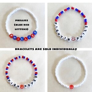 May include: Four beaded bracelets. One white bracelet with red and blue beads spelling "PHILLIES" and another with "FIGHTIN PHILS". A third bracelet spells "HIGH HOPES". The fourth bracelet is white with a red smiley face bead. Text: "BRACELETS ARE SOLD INDIVIDUALLY".