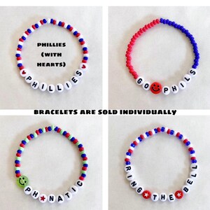 May include: Four beaded bracelets in red, white, blue, and green. Each bracelet features white letter beads spelling out phrases like "PHILLIES" and "RING THE BELL". Some bracelets include smiley face and star beads.