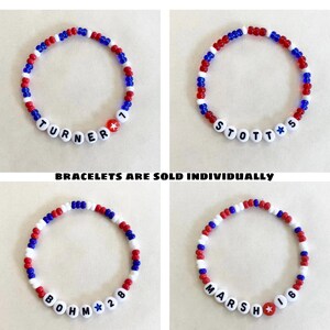 May include: Four beaded bracelets with red, white, and blue beads. Each bracelet has a name and number spelled out with white letter beads. The text "BRACELETS ARE SOLD INDIVIDUALLY" is at the bottom of the image.