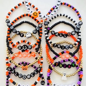 May include: A collection of beaded bracelets featuring Halloween themes with orange, black, white, purple, and gold beads. The bracelets include letter beads spelling phrases like Happy Halloween, Spooky Szn, Trick or Treat, Boo, and Hocus Pocus.