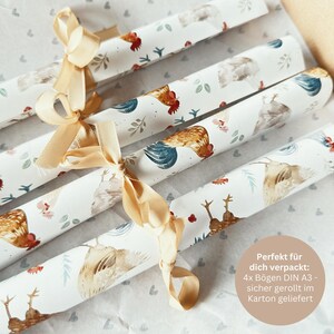 May include: Four rolls of white wrapping paper with a chicken and floral pattern. The rolls are tied together with a beige ribbon. The text on the paper reads "Perfekt f&uuml;r dich verpackt: 4x B&ouml;gen DIN A3 - sicher gerollt im Karton geliefert".