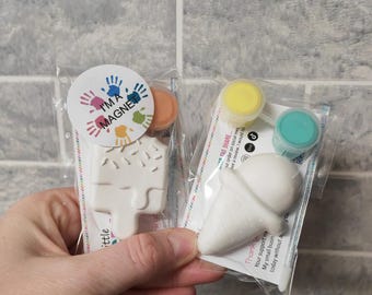 Puede incluir: Dos adornos de cerámica blanca para pintar, uno con forma de cono de helado y el otro con forma de paleta de helado. Ambos vienen con pequeños recipientes de pintura y un imán.