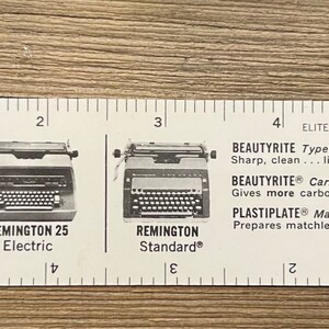 May include: A white plastic ruler with a black and white image of two Remington typewriters. The ruler has markings for inches and includes the text "By any measure - Remington typewriters and supplies are the finest in the land!" and "BEAUTYRITE Typewriter Ribbon, BEAUTYRITE Carbon Paper, PLASTIPLATE Masters".