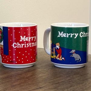 May include: Set of four white ceramic mugs with a Christmas theme. Each mug features a different design with a red, green, or blue background and a festive scene. The mugs all say "Merry Christmas" in red lettering.