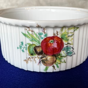 May include: White ceramic baking dish with a fluted rim and a painted design of vegetables, including a red tomato, green leaves, and a brown onion.