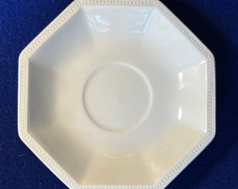 May include: White octagonal saucer with a beaded edge. The saucer is made of ceramic and has a smooth, glossy finish.