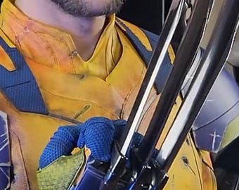 Può includere: Una persona con un costume giallo e blu con artigli argentati. Il costume ha un top giallo con dettagli blu. Gli artigli sono lunghi e metallici. La persona guarda direttamente la fotocamera.