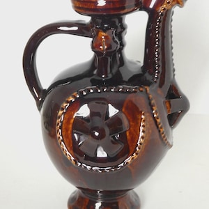 Peut inclure: Pichet en céramique marron avec une anse et un bec verseur original. Le pichet présente un motif décoratif en forme de croix sur le devant et est recouvert d'un vernis brillant. Le socle est de style piédestal.