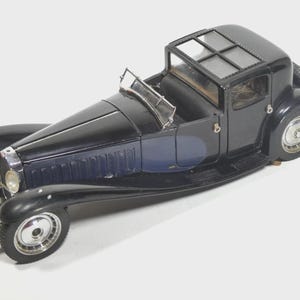May include: A detailed model of a classic black car with a blue accent on the side. The car features a convertible top with a glass roof, chrome wheels, and a spare tire on the back. The model is a vintage collectible.