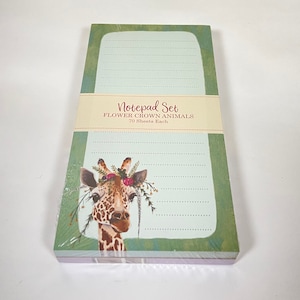 May include: A set of two green and purple notepad sets with a giraffe wearing a flower crown on the front. The notepad set is titled "Notepad Set Flower Crown Animals 70 Sheets Each".