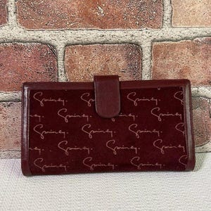 May include: A rectangular burgundy suede clutch wallet featuring a repeating script pattern of the word "Griney" in a lighter shade. The wallet includes a central vertical strap with a snap closure and smooth leather trim along the edges.