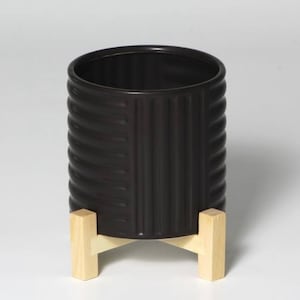 May include: Black ceramic planter with a ribbed design, sitting on a wooden stand with four legs.