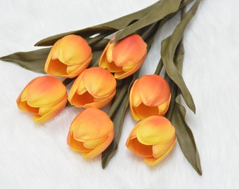Pode incluir: Um ramo de sete tulipas artificiais de cor laranja e amarela com caules e folhas verdes.