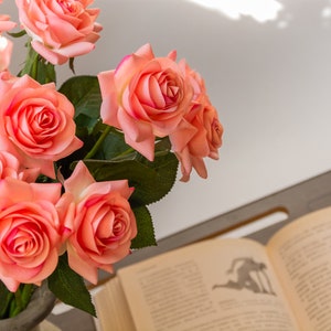 May include: A bouquet of pink roses in a vase, with a book open on a table in the background.