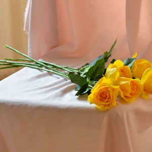 Pode incluir: Um buqu&ecirc; de rosas amarelas com caules e folhas verdes, descansando sobre uma superf&iacute;cie de tecido rosa.
