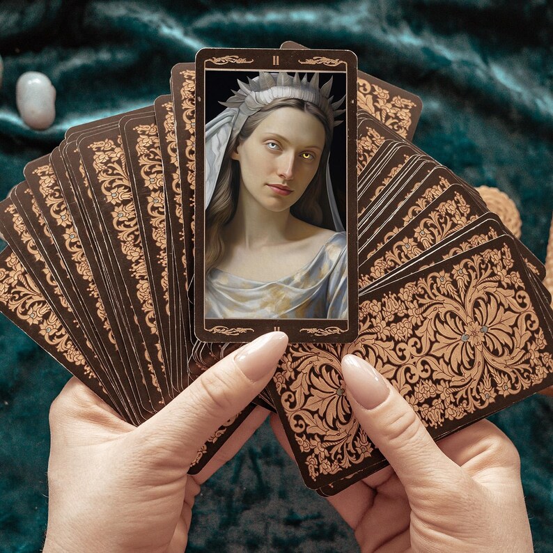 May include: A tarot card deck featuring a central card with a portrait of a woman wearing a crown and veil. The other cards have a brown and gold floral design. The cards are held in a person's hands against a dark green background.