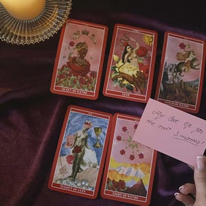 May include: A collection of tarot cards with red borders and various illustrations. The cards include "Queen of Wands," "Lust," "Witch of Wands," "Maiden of Cups," and "Eight of Wands." A pink note reads "My love life for the next 3 months?"