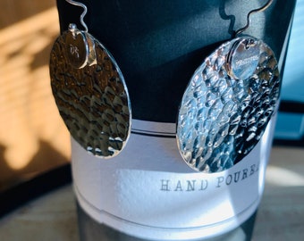 Puede incluir: Un par de pendientes de plata con textura martillada. Los pendientes son de forma ovalada y tienen un pequeño dije redondo unido a cada uno. Los dijes están grabados con las palabras "Dreamer" y "DR".