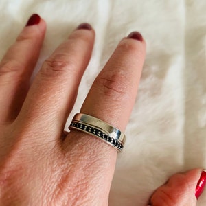 May include: A silver band ring with a row of black stones set into the band.