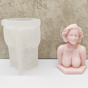 Puede incluir: Un busto de resina rosa de una mujer con el pelo rizado. El busto está sobre una base hexagonal. También se muestra en la imagen un molde de silicona transparente.