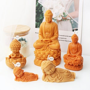 May include: Set of five golden Buddha candles, each depicting a different pose. The candles are made of wax and have a detailed design. The candles are arranged on a white surface.