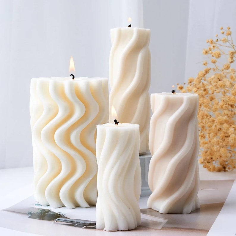 K&ouml;nnte beinhalten: Vier wei&szlig;e und cremefarbene Kerzen mit einem wellenf&ouml;rmigen Design. Die Kerzen sind auf einer wei&szlig;en Oberfl&auml;che angeordnet.
