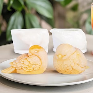 May include: Two yellow bird-shaped silicone moulds on a white plate. The moulds are detailed with feathers and have a realistic bird design.