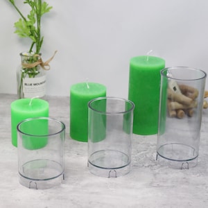 Puede incluir: Cuatro moldes de velas de plástico transparente de diferentes tamaños. Los moldes están vacíos y están sobre una superficie gris. Hay tres velas verdes en los moldes.
