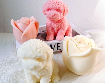 May include: Three handmade soap sculptures: a pink poodle, a white poodle, and a white rose. The soaps are sitting on a book with the word "Love" visible.