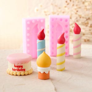 Può includere: Una collezione di decorazioni colorate in miniatura a tema compleanno. Include una piccola torta con la scritta "happy birthday", oggetti a forma di candela con fiamme rosse e stampi rosa. Le candele hanno accenti blu, gialli e rosa.