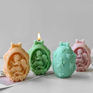May include: Four decorative Easter egg candles with a floral design and an angel figure. The candles are in shades of pink, green, and peach.