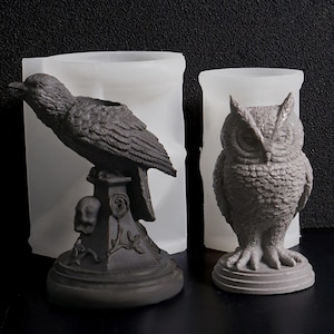 May include: Two grey resin moulds: a raven perched on a pedestal with a skull and an owl. The raven mould is angled, while the owl mould is upright. Both are set against a white background.