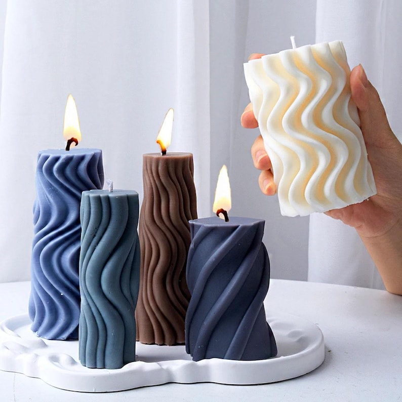 K&ouml;nnte beinhalten: F&uuml;nf dekorative Kerzen mit einem wellenf&ouml;rmigen Design. Die Kerzen sind in den Farben Blau, Braun und Wei&szlig;. Die Kerzen stehen auf einer wei&szlig;en Oberfl&auml;che.