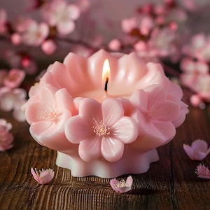 May include: A pink candle shaped like a flower with five petals. The candle is lit and the flame is visible. The candle is surrounded by pink flower petals.