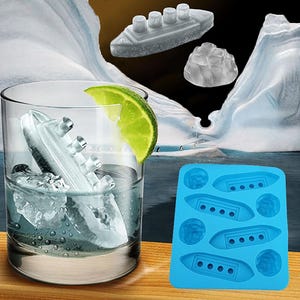 Op de afbeelding: Een helder glas gevuld met water en ijsblokjes in de vorm van een schip, met een schijfje limoen. Een blauwe siliconen ijsvorm met scheepsvormige holtes is ook zichtbaar. Ijsbergen zijn op de achtergrond.