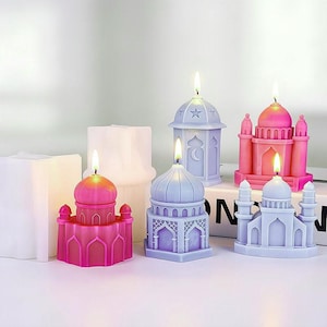 May include: A collection of colorful mosque-shaped candles with lit wicks. The candles are in shades of pink, purple, and blue. Some candles have star and moon designs. The candles are on a white surface.