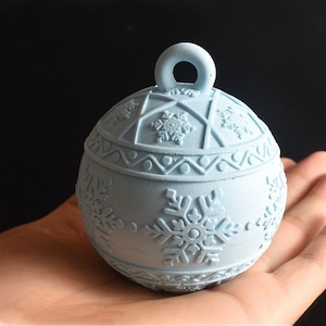 Op de afbeelding: Een lichtblauwe kerstbal van keramiek in de vorm van een bal met een sneeuwvlokkenpatroon. De bal heeft een lus aan de bovenkant om op te hangen.