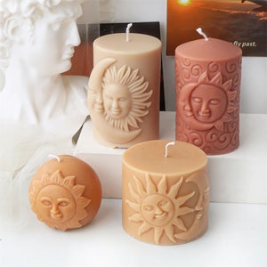 May include: Four candles with a sun and moon design. The candles are in different colours and sizes. The candles are on a white surface. "Fly past." is written on a card in the background.