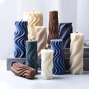 Peut inclure: Assortiment de bougies décoratives de différentes couleurs et designs. Les bougies sont toutes à motifs ondulés et sont en cire. Les bougies sont disposées sur une table avec une surface en bois.