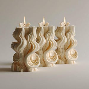 May include: Three white, intricately sculpted candles with a wavy, organic design. The candles are lit and the flames are visible.