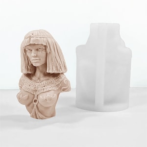 Può includere: Un busto in scultura beige di una donna con i capelli lunghi che indossa una collana decorativa. La scultura è accanto a uno stampo in silicone bianco.