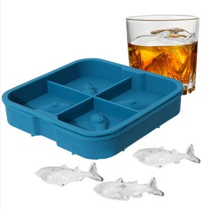 May include: A blue silicone ice cube tray with four compartments, each shaped like a fish. Three fish-shaped ice cubes are visible, along with a glass of amber liquid containing a fish-shaped ice cube. The tray is designed for making novelty ice cubes.