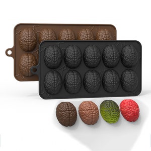 May include: Two silicone molds for making chocolate brains. The top mold is brown and the bottom mold is black. There are four chocolate brains in different colors: brown, red, green, and brown.